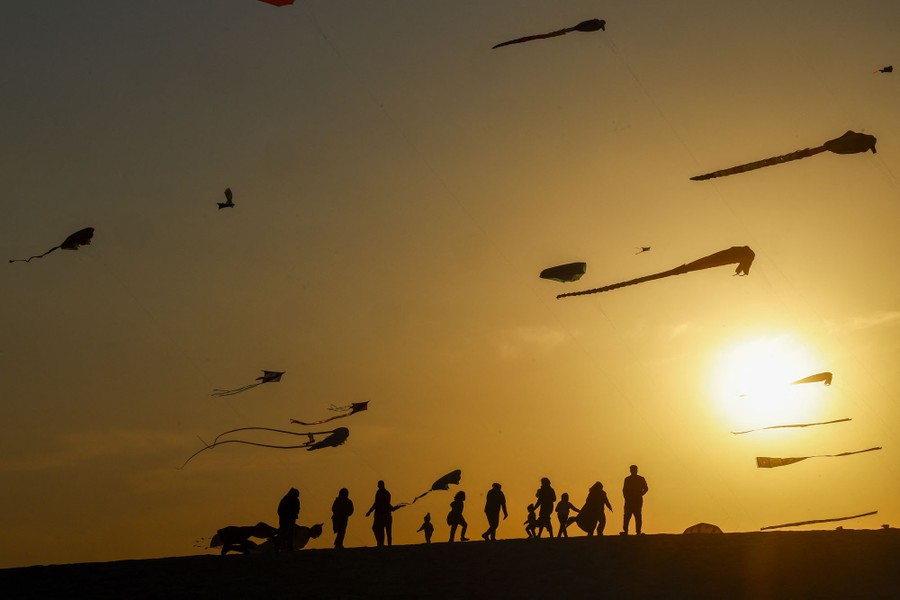 About a dozen people are gathered beneath multiple kites in the air above.