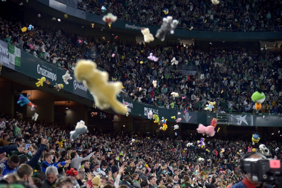 Stuffed animals fall to the floor of a stadium, thrown by hundreds of fans.