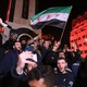 A crowd chants and waves flags in a city square at night.