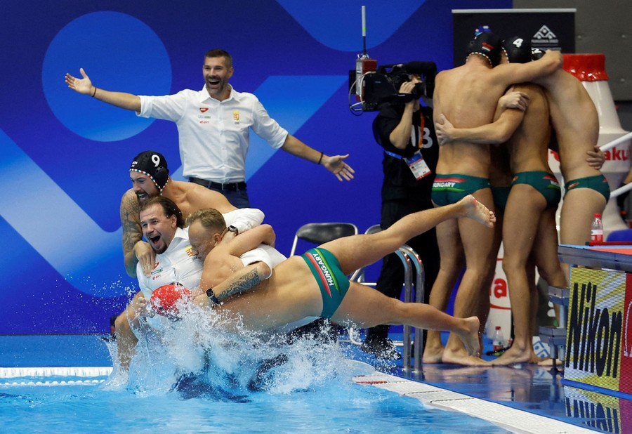 Several water polo players and coaches jump into a pool, celebrating.