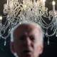 A photo of Joe Biden, blurred in foreground, in front of a chandelier in focus behind.