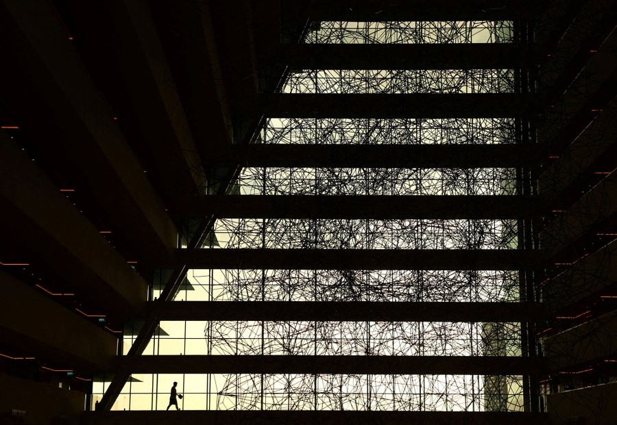 A man walks inside a large hotel atrium, with many tall windows in the background.