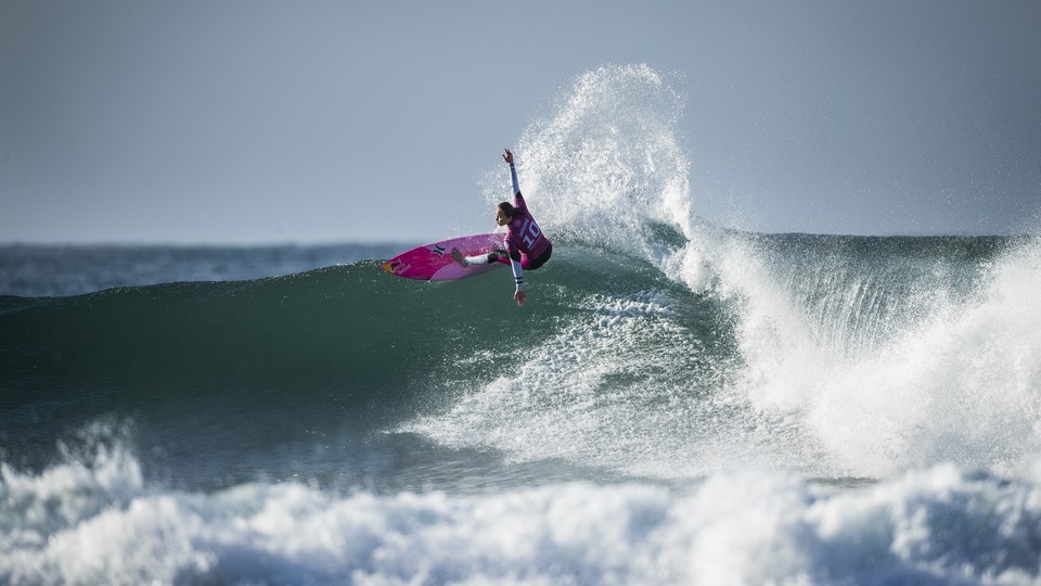 a photo of surfer in pink at the crest of a wave