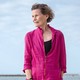 Woman in magenta top and black capri pants standing barefoot on beach with cloudy blue sky behind