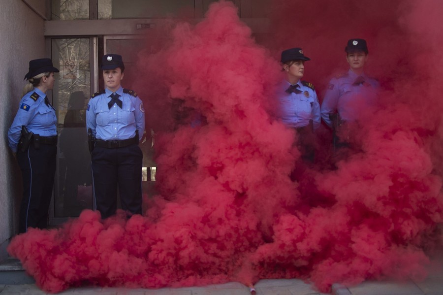 At least four police officers stand outside a building, enveloped in thick red smoke.