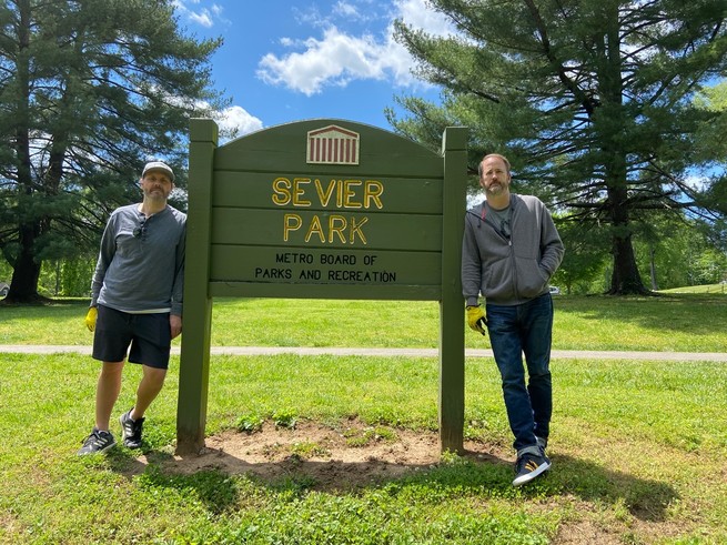 Gabe Scott and Andy Gullahorn stand in a park, leaning on a sign that reads "Sevier Park"