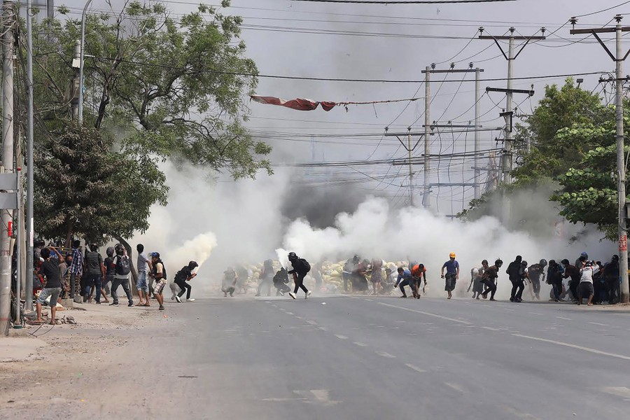 People run in a street, away from white clouds of tear gas.
