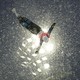 A skier is seen in mid-air during a jump, backlit by spotlights, amid a snowstorm.