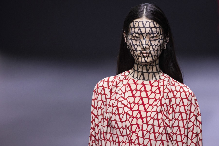 A model wears a patterned garment, with a matching pattern painted on their face.