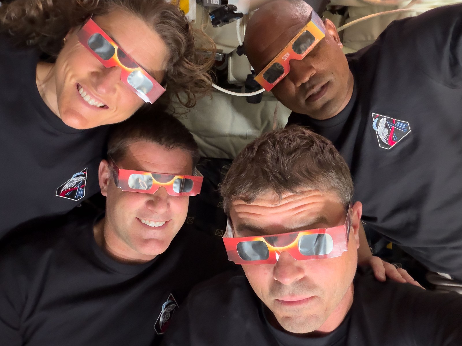The four-person crew of Artemis pose for a photo, all wearing eclipse glasses.