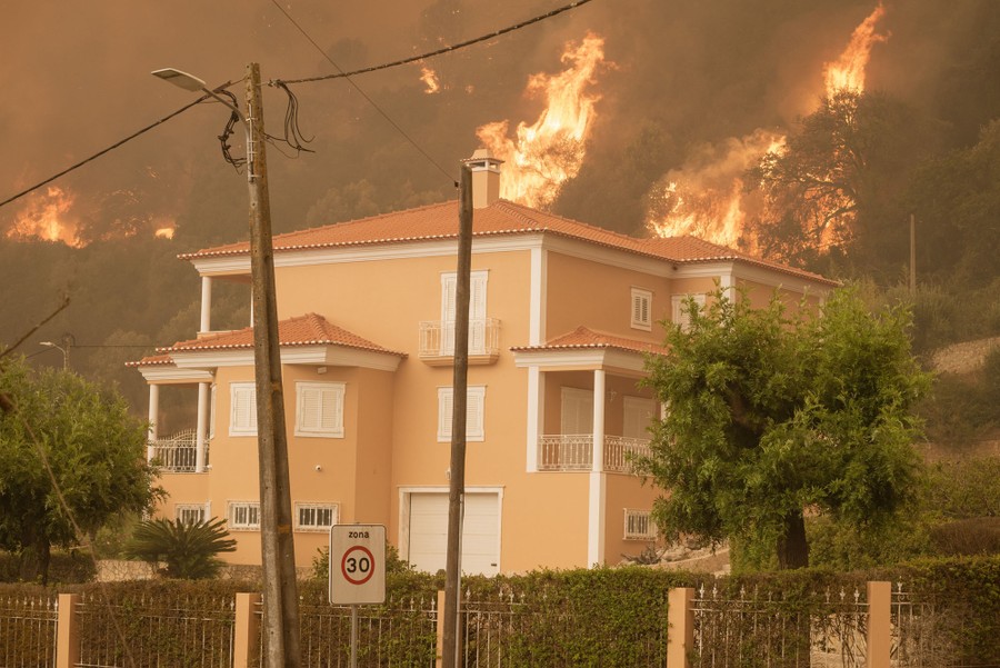 A wildfire on a hillside burns near houses.