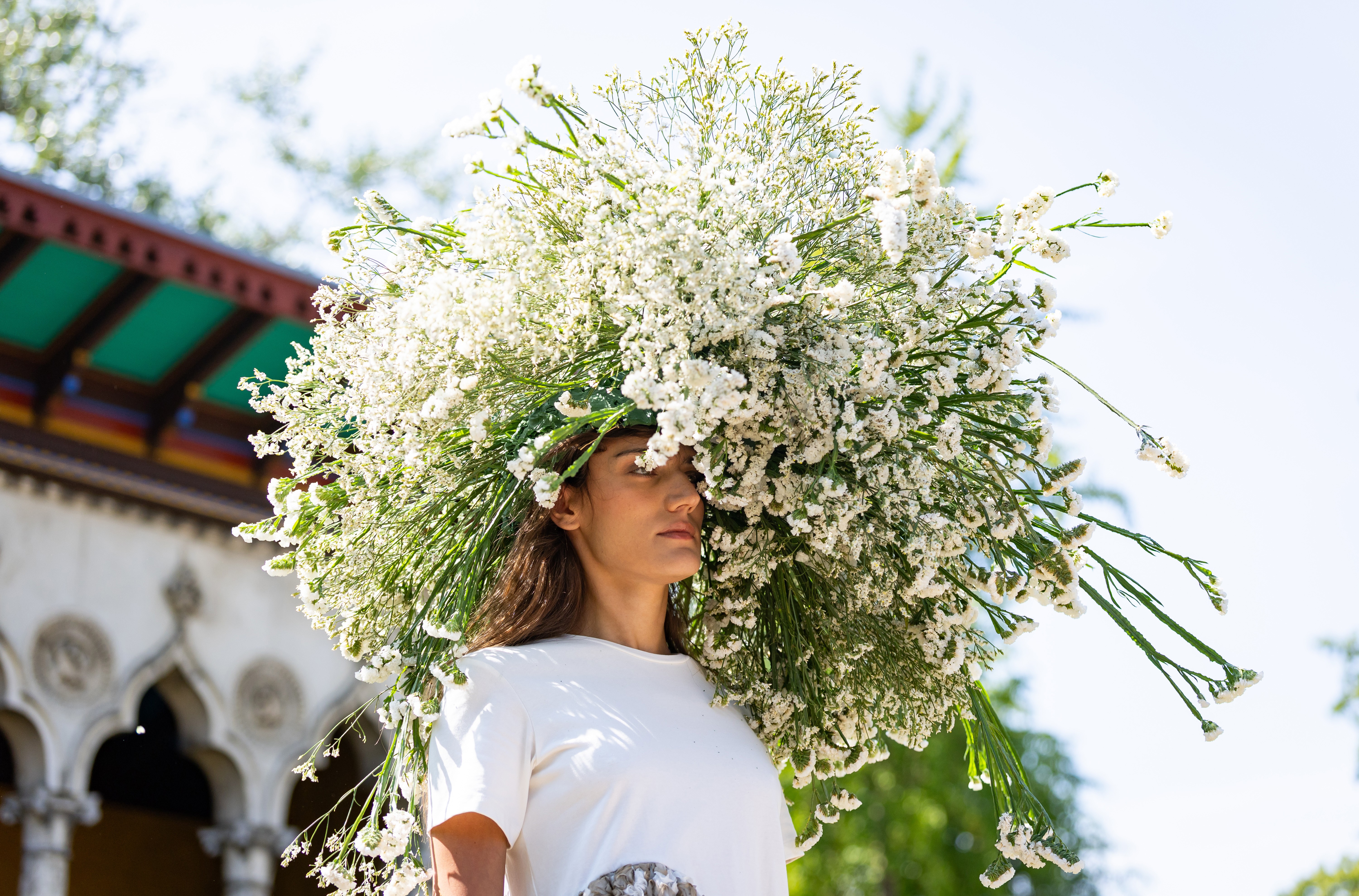 A model wearing a large floral arrangement on their head walks on a runway.