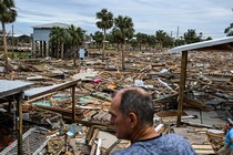 A man in the foreground looks at splinters of structures strewn on the ground amid palm trees after Hurricane Helene struck the Gulf Coast.