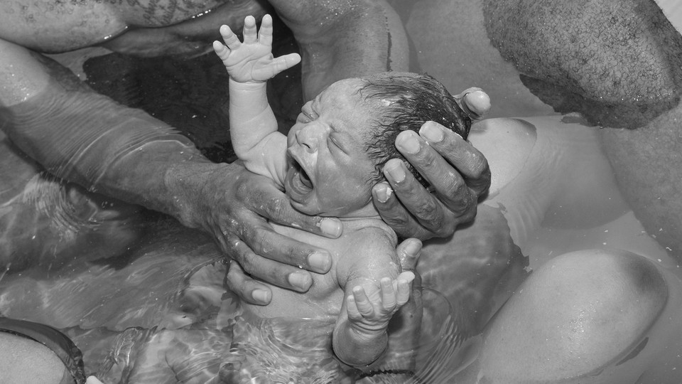A newborn baby being held up in water