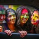 Four people with colored powder all over their faces smile and pose side by side.