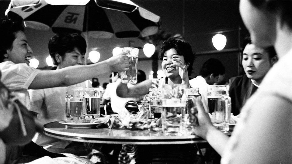 a black-and-white image of Asian women, seated around a table, toasting each other with mugs of beer