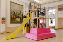 A colorful playground with a slide is placed in an old ballroom.
