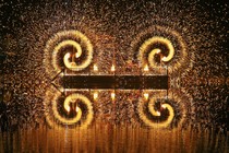 Spinning fireworks, mounted to stands, throw out two spirals of sparks, reflected in a pond.