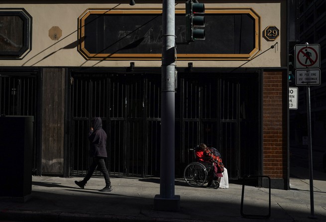 A person in a wheelchair is seen in the shadows on a street in San Francisco while anoter person walks by