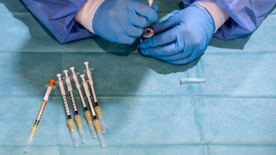 gloved hands load a vaccine into a syringe, next to an array of other vaccine syringes