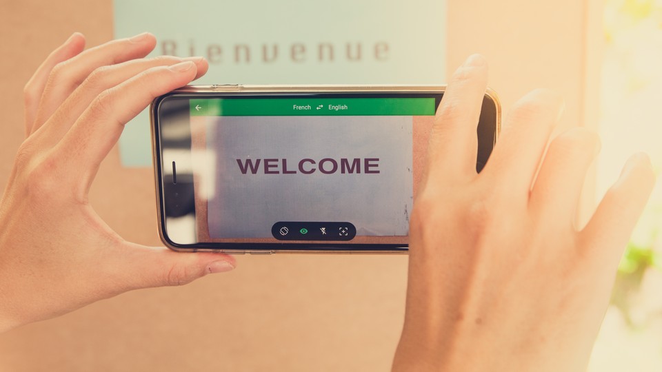 Hands hold a smartphone in front of a sign saying "Bienvenue," and the smartphone reads "Welcome."