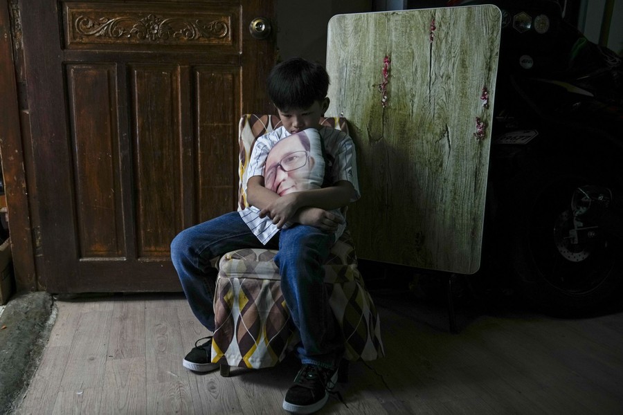 A boy sits in a chair holding a pillow with the face of his late father printed on it.