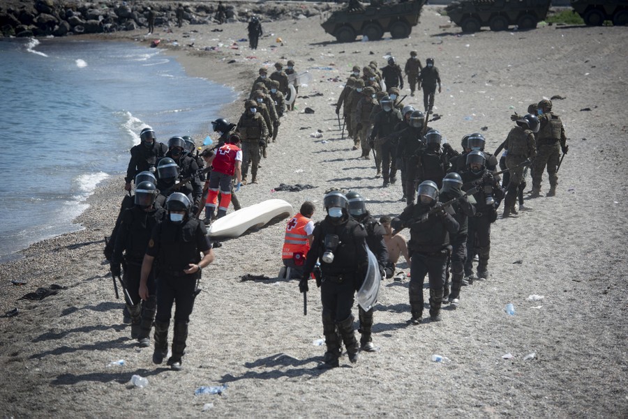 Dozens of soldiers in riot gear walk on a beach.
