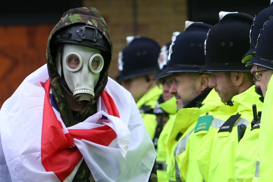 A protester in a gas mask walks in front of a line of police officers.