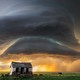 A huge storm cloud swirls above a wide open plain, with a small broken-down shack in the foreground.