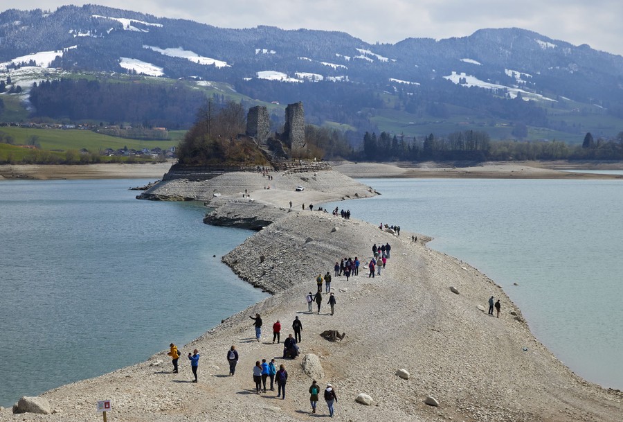 People walk along a path toward a castle in a lake.