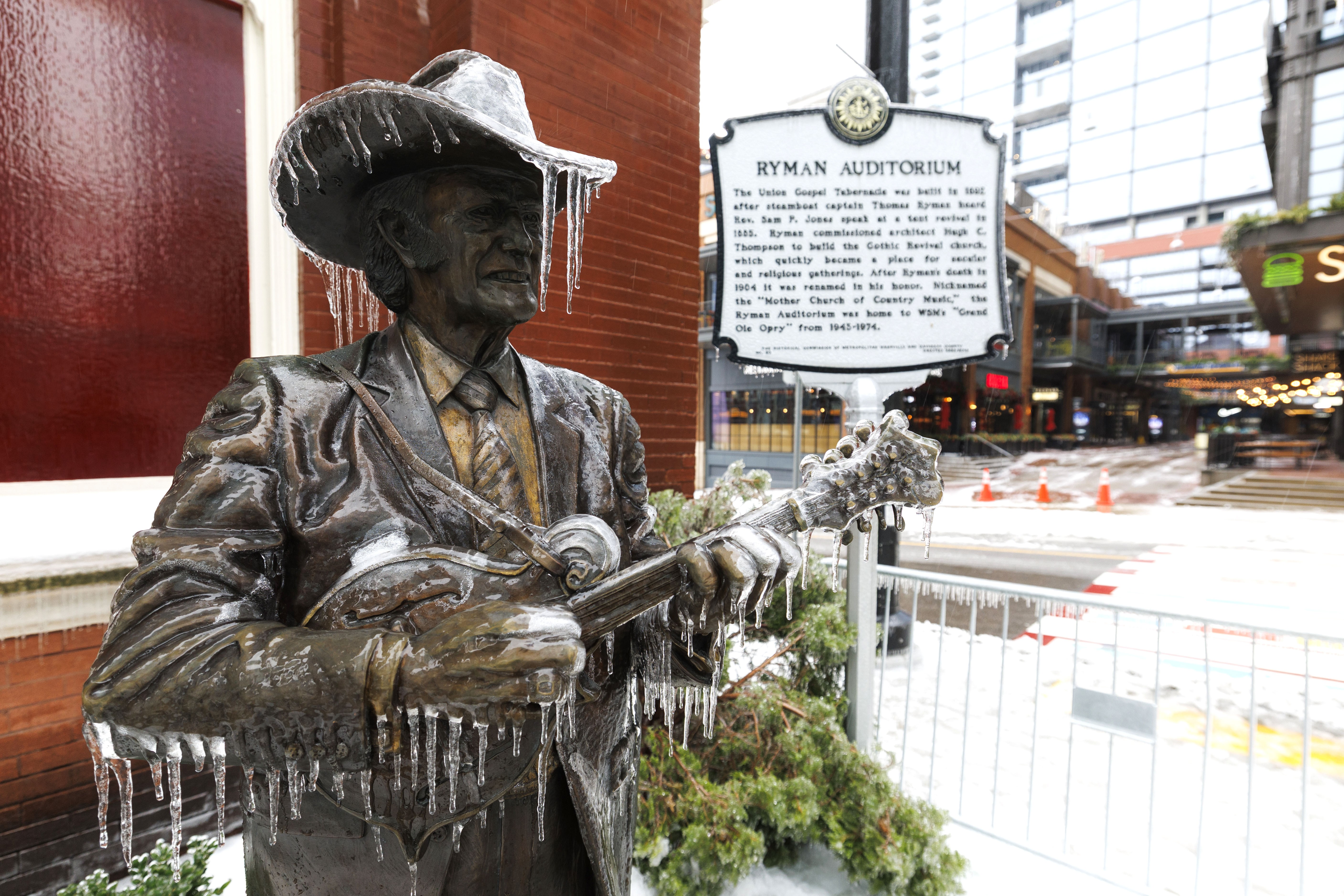 A bronze statue of a bluegrass singer stands outside an auditorium, covered in ice.