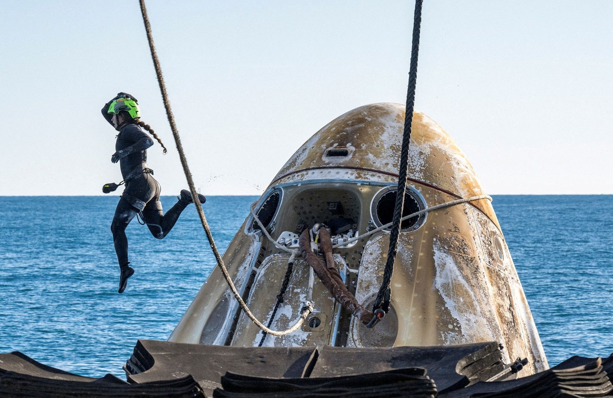 A diver leaps into the ocean from a floating space capsule.