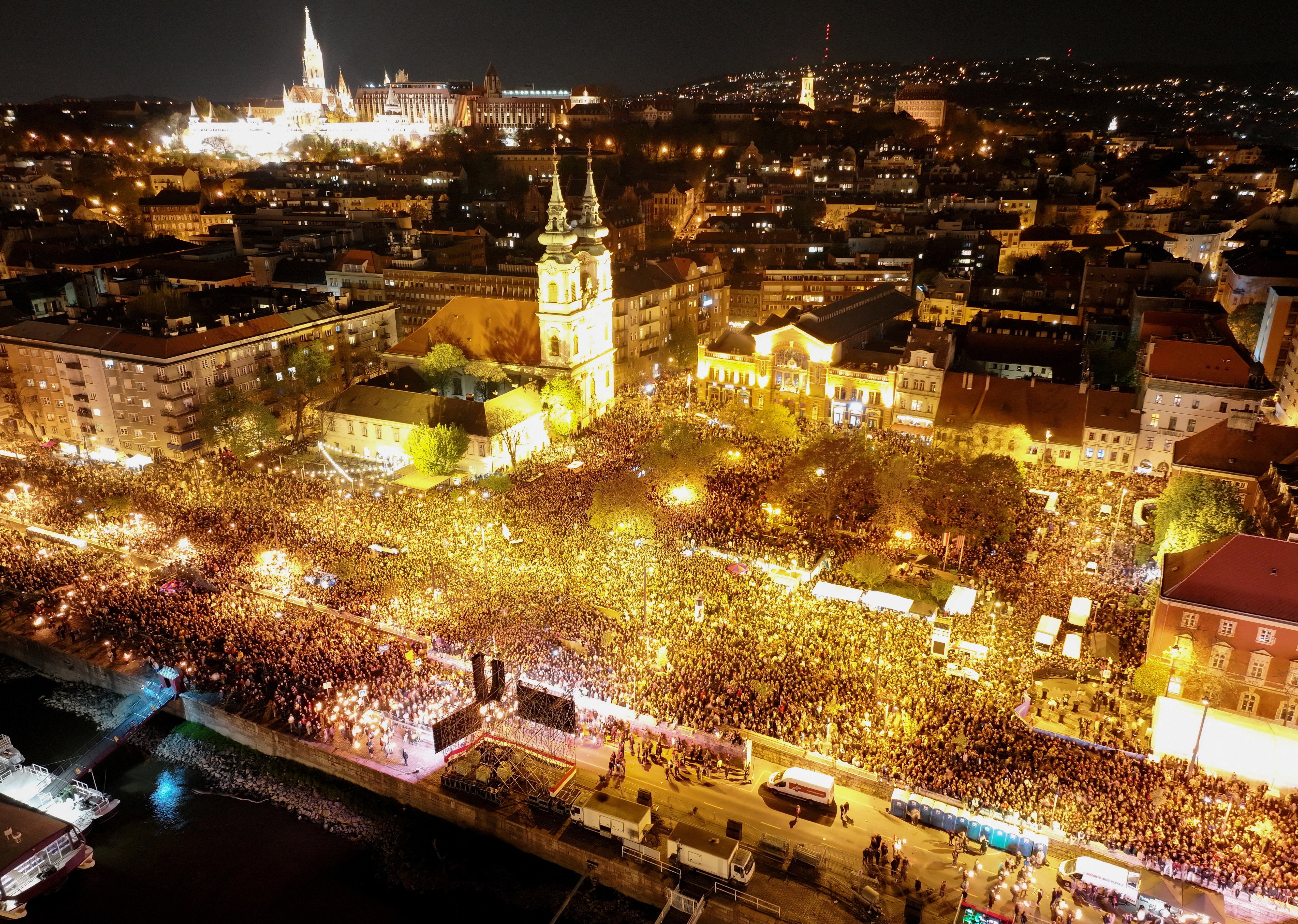 A drone view of a large crowd gathering to celebrate alongside the River Danube in Budapest, at night.