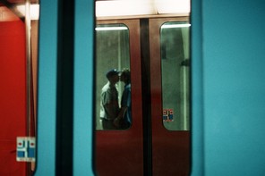 A photograph taken through subway train car doors, looking into another set of train car doors passing by, and a blurry couple holding hands and kissing inside that train