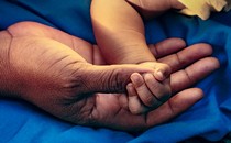 A baby's hand holds an adult's thumb