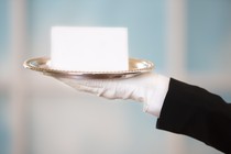 White gloved hand in black suit holds a blank notecard on a silver platter.