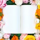 An open blank book surrounded by roses and other flowers