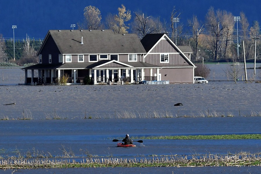 A person kayaks on a flooded stretch of farmland.
