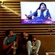 Two Iraqi youths stare at a TV showing an image of Abu Bakr al-Baghdadi.