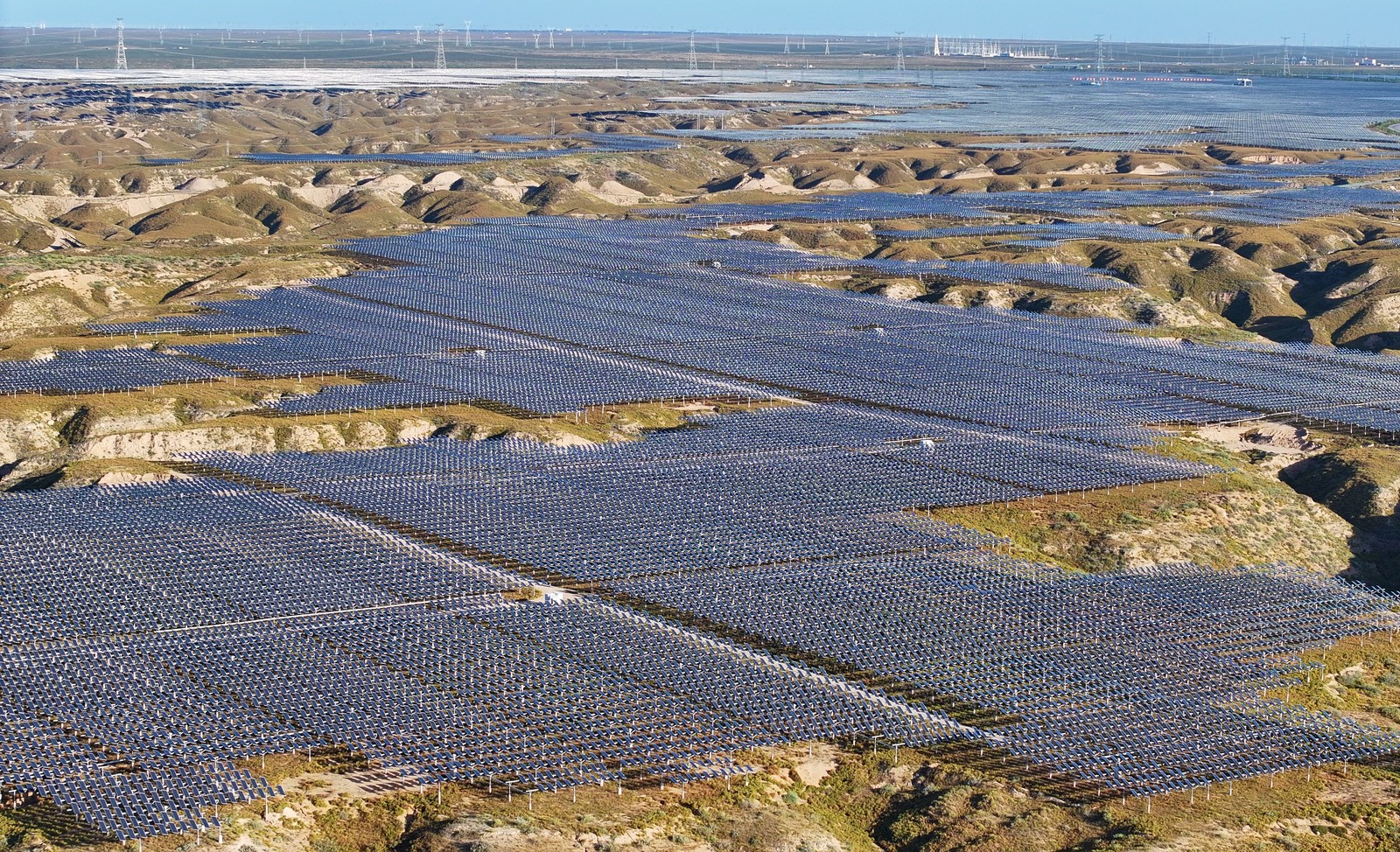 An aerial view of an uneven landscape, where the flat parts are covered by acres of solar panels