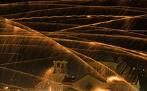 Streaks of light in the night sky above a church, evidence of several firework rockets flying past.