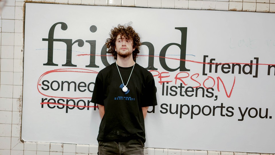 A man with curly hair stands in front of a billboard at a subway station.
