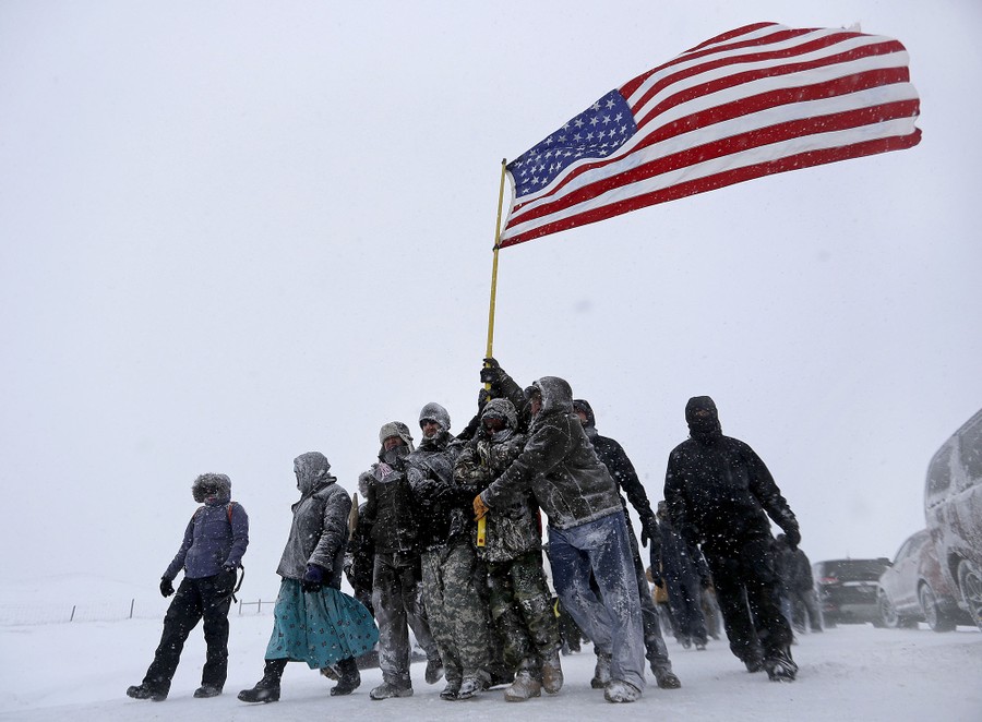 Military veterans huddle together to hold a United States flag against strong winds during a march to a closed bridge outside the Oceti Sakowin Camp on December 5, 2016.