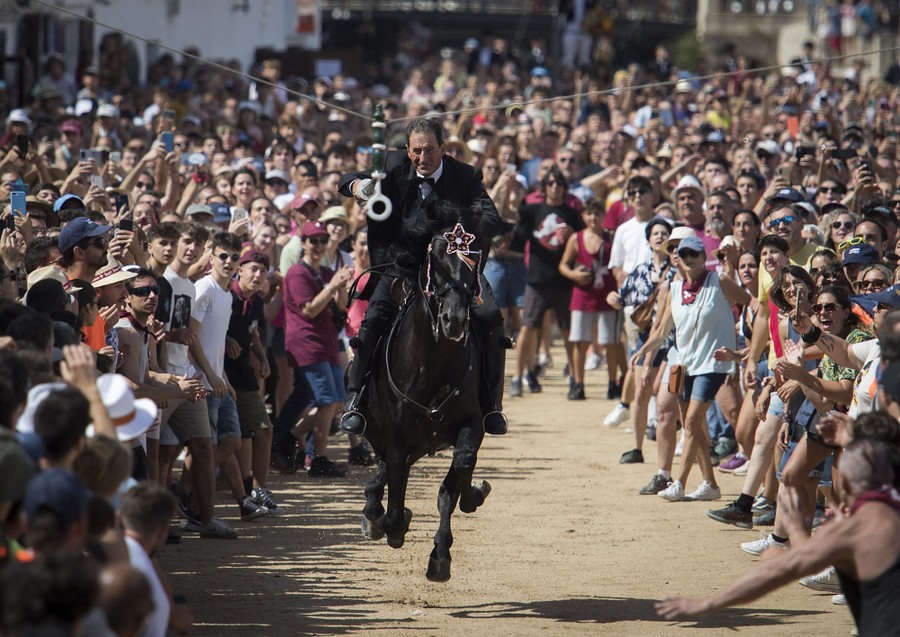 A horse and rider gallop through a narrow open space in a crowded town square.