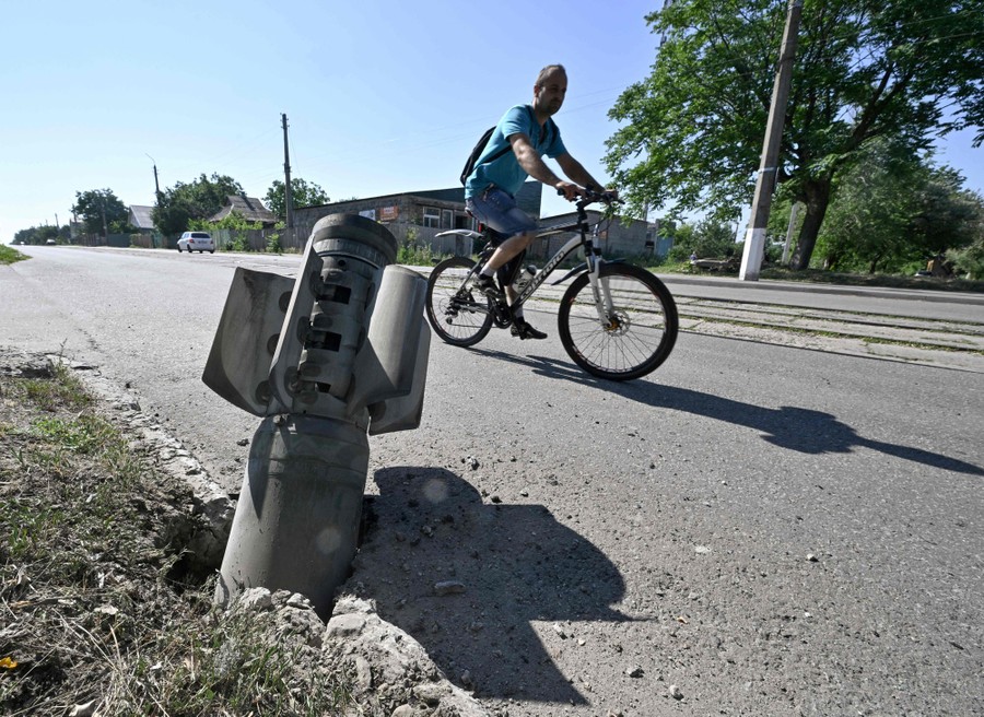 A cyclist rides past the tail section of a rocket embedded in a road.