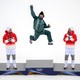 A skier jumps up, fist held high, smiling, as he climbs atop a podium to receive a gold medal, flanked by the bronze and silver winners.
