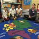 Children sit on a colorful rug decorated with a map and animals.