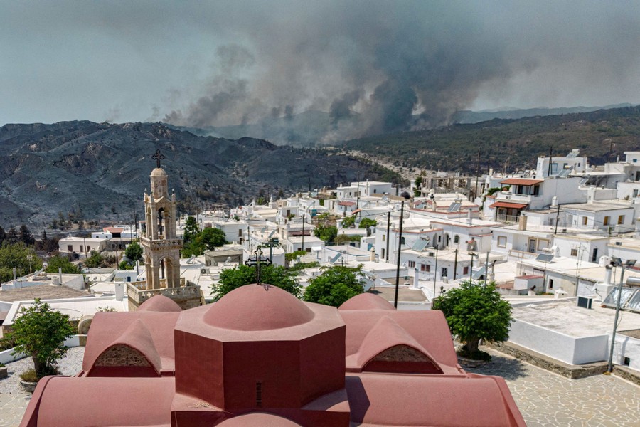 A view from a hillside village, looking out toward a wildfire burning in the distance.