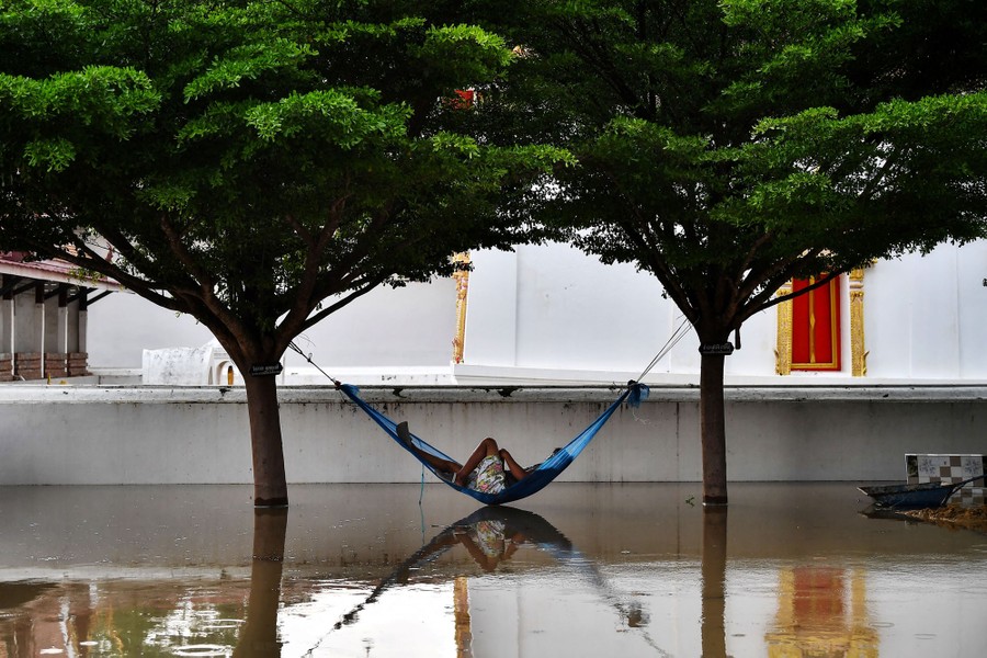 A man lies in a hammock suspended above floodwater.