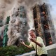 A man reacts emotionally while standing outside a burning complex of tall residential buildings.